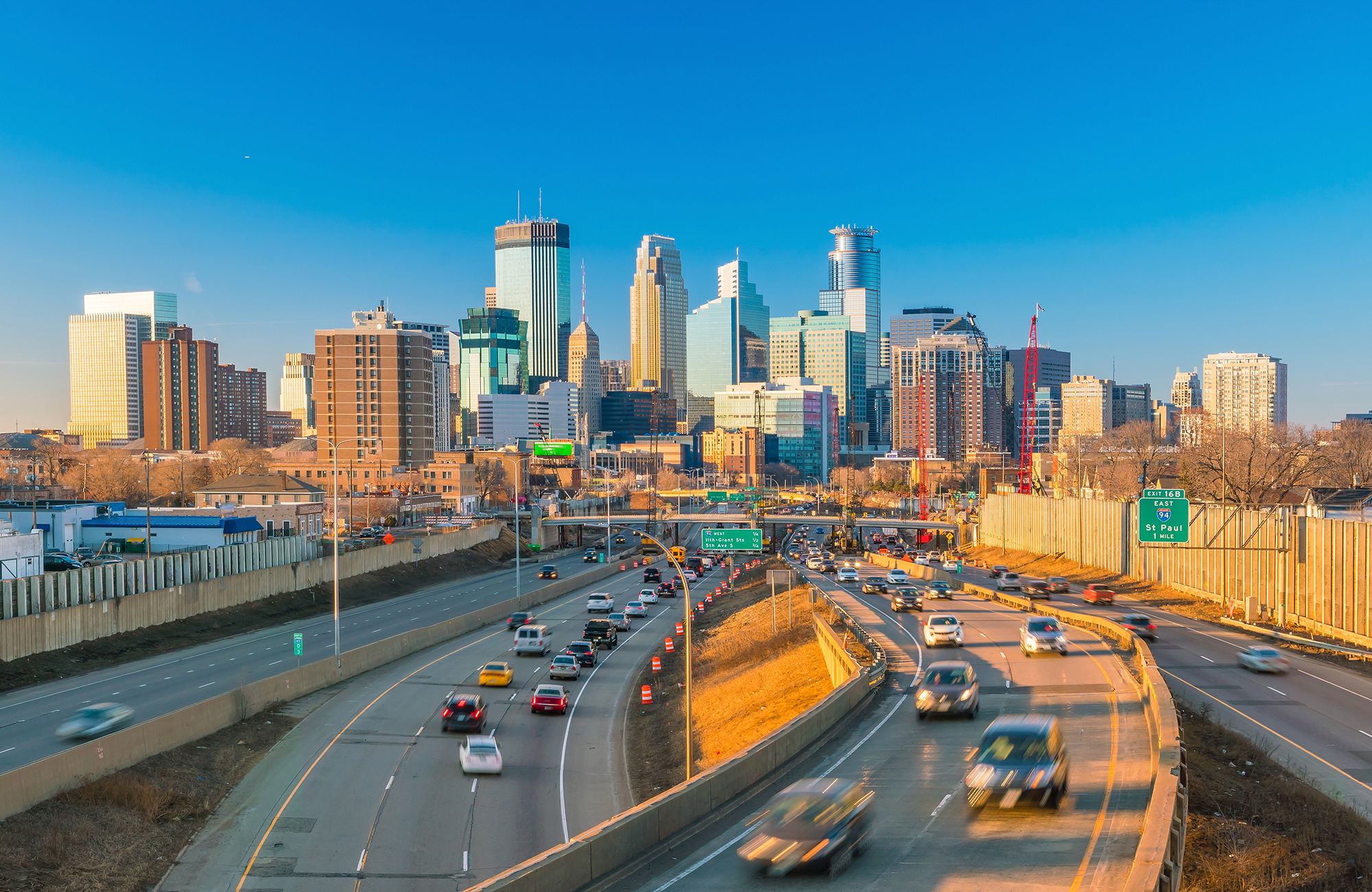 Busy highways into Minneapolis, with the skyline of the city against a bright blue sky
