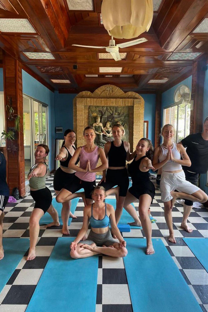 Freja and six other girls, standing and sitting on blue mats in a yoga retreat in Thailand