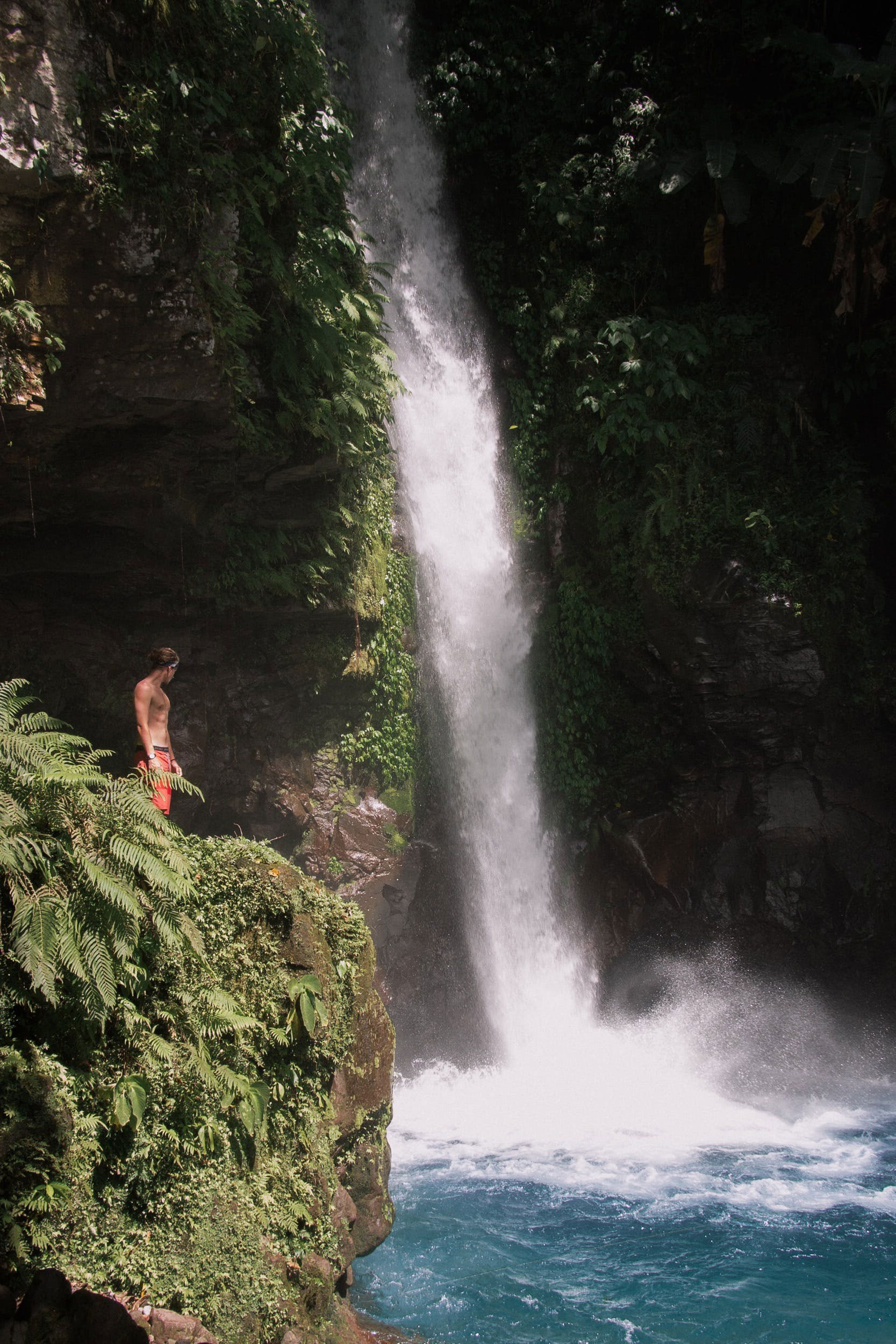Guy in his swimshorts standing on rocks near a waterfall in Hinatuan, on Mindanao in the Philippines
