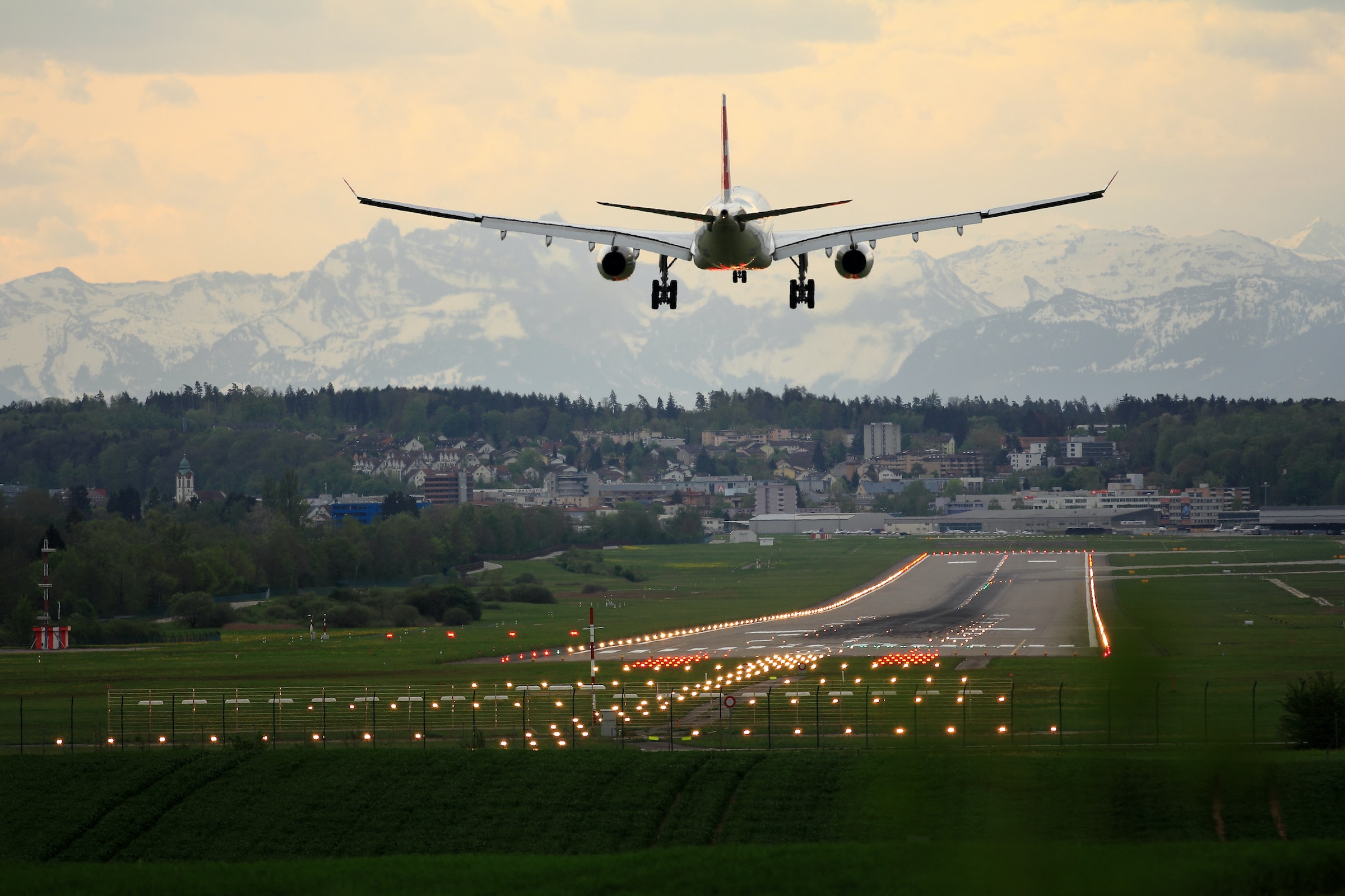 Airplane landing at an airport during sunset, with snow-covered mountains in the background.