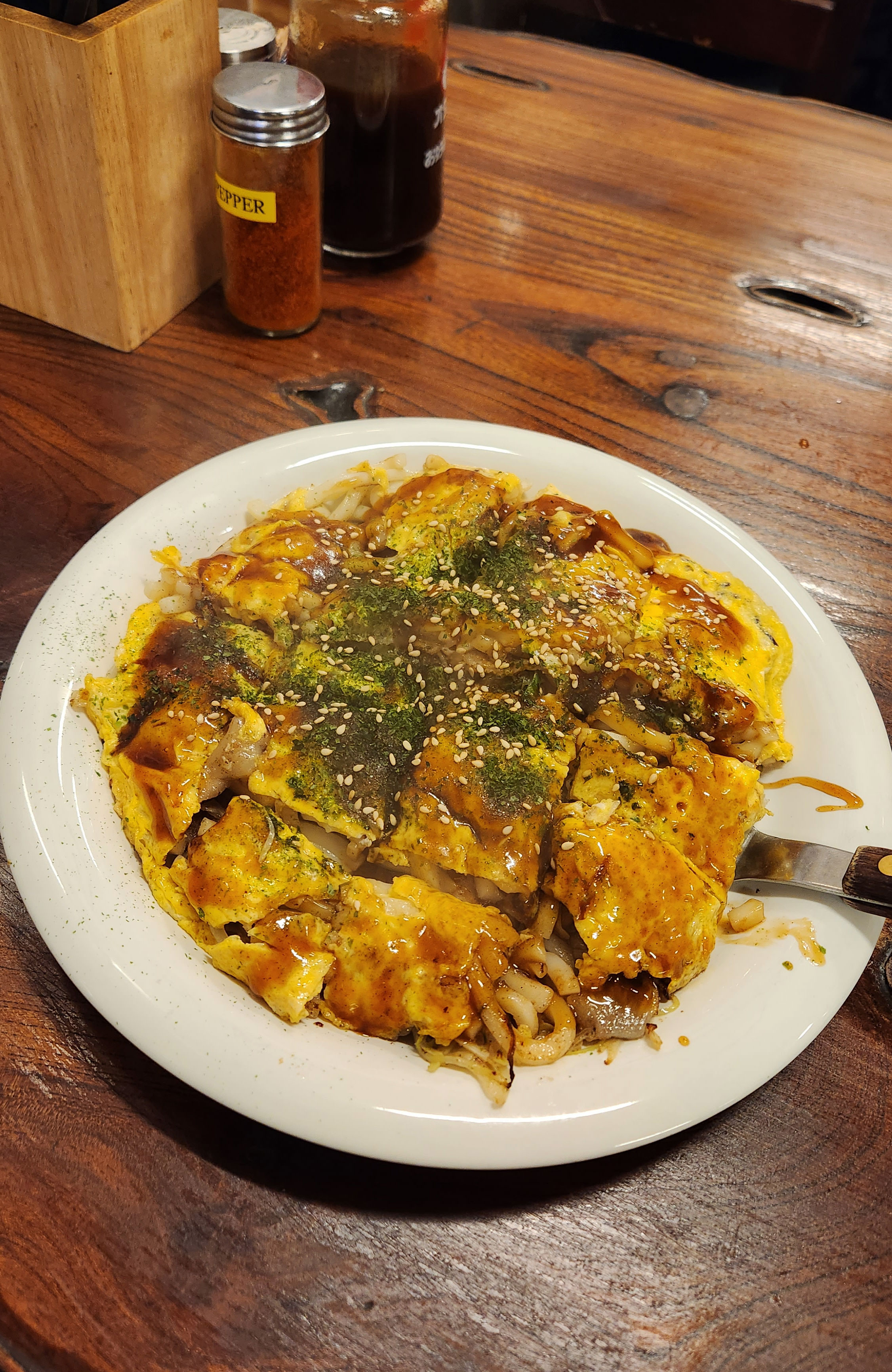 Platter of okonomiyaki, a savory pancake/omelett crossover with noodles, vegetables and sauce. 